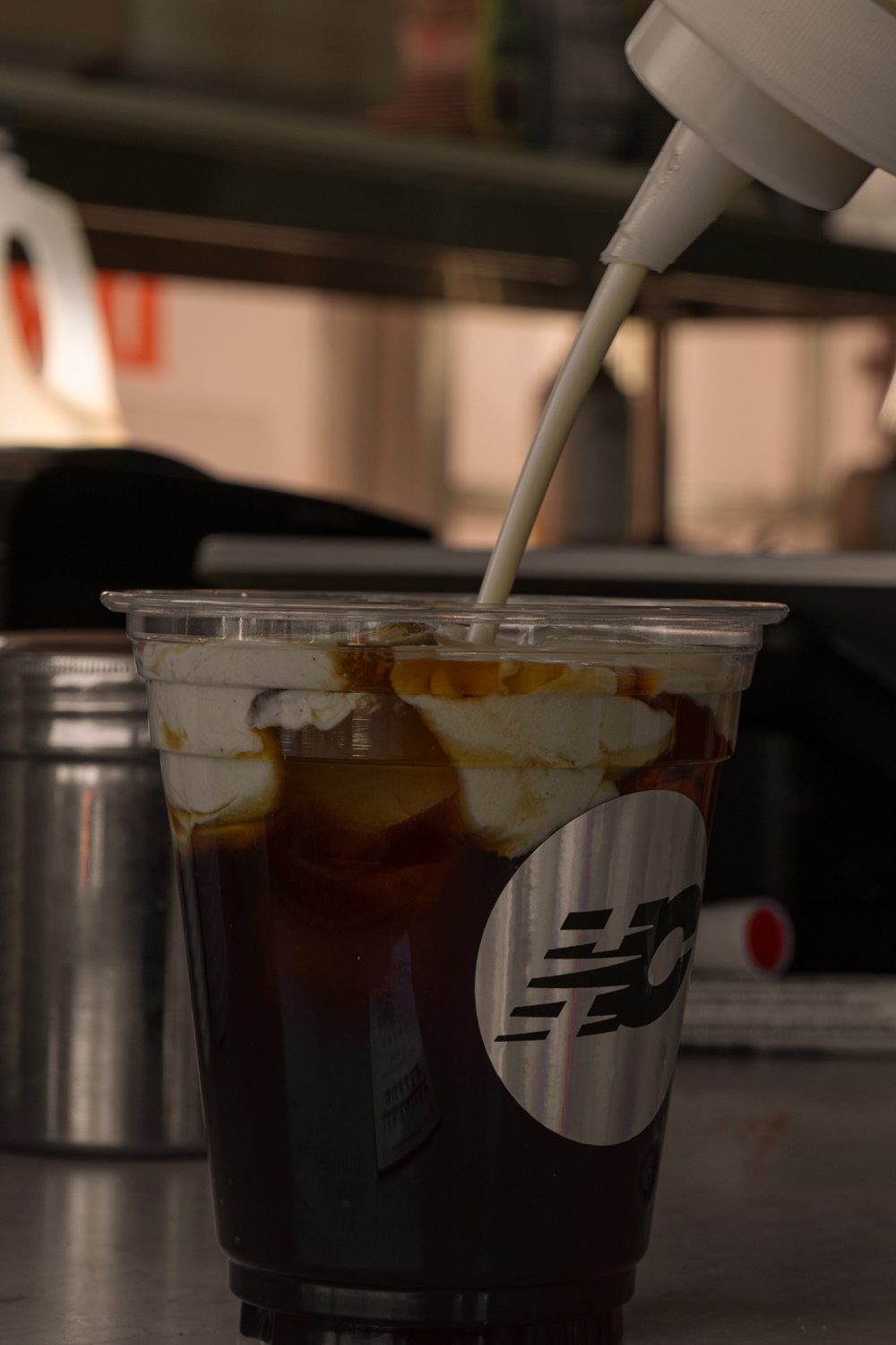 Cream being poured into an iced coffee in a branded HC cup